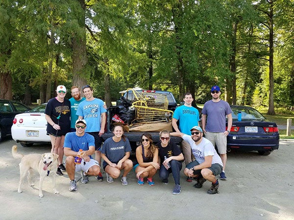 Group of students standing in front of cars with a dog