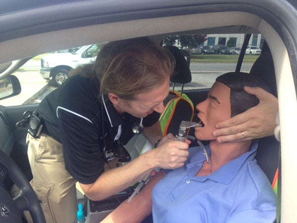 Student examining a training mannequin in a car