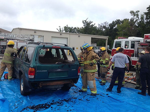 Students in firefighter uniforms breaking into a car