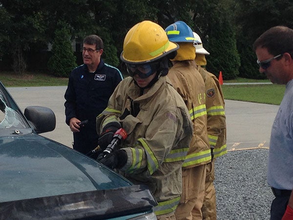 Student in firefighter uniform with safety goggles cutting into a car