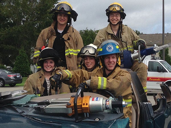 Students in firefighter uniforms sitting inside of a car after they cut off the roof