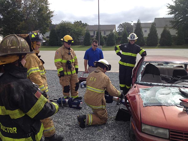 Students wearing firefighter uniforms cutting apart a car